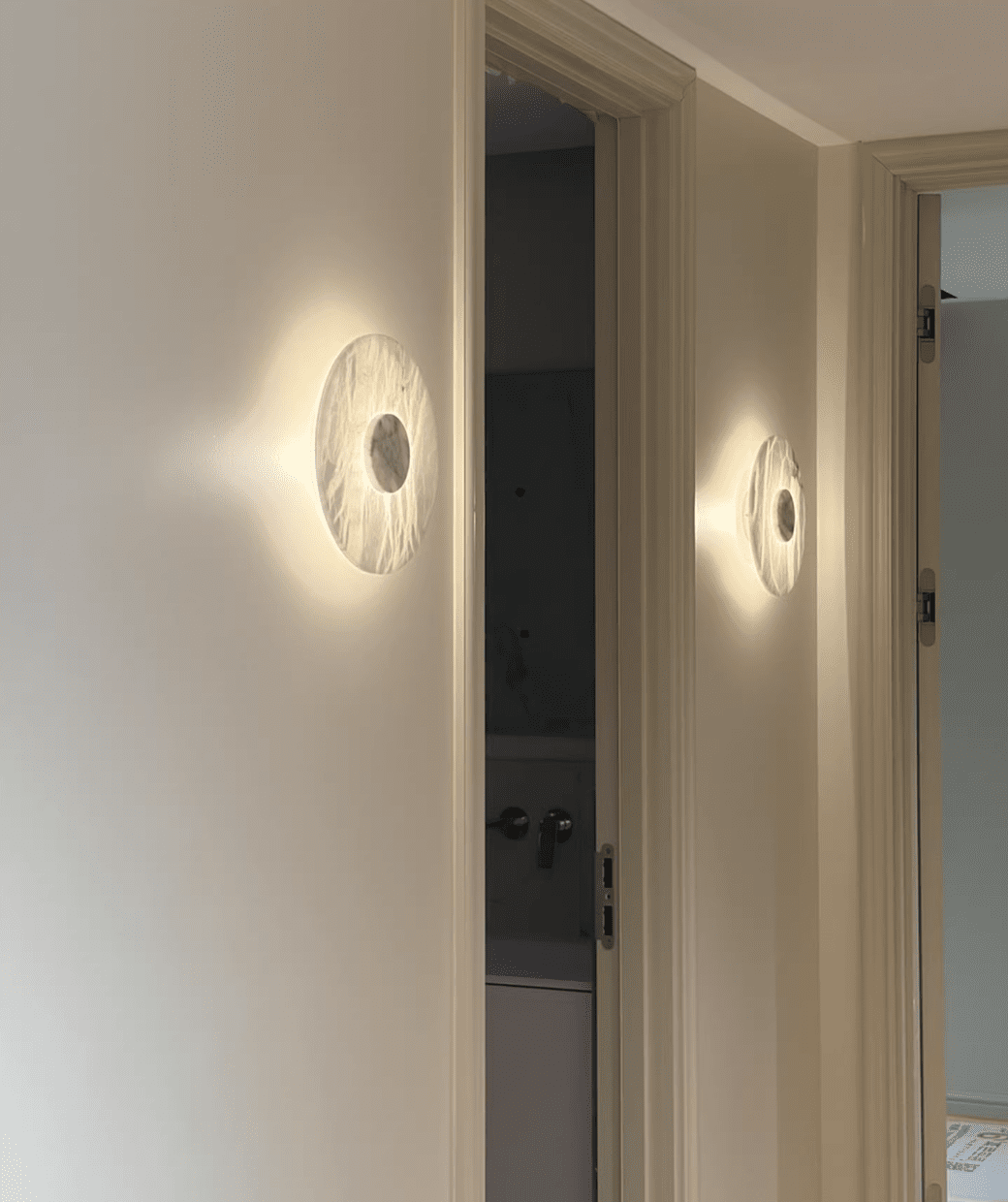 Two Clérachic alabaster wall lights glow along a hallway wall beside two panelled doors leading to further rooms.