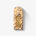 An arched marble wall sconce from Clérachic glows softly along its veined edges around a brushed brass centre panel, photographed alone on a plain backdrop.