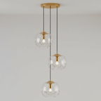 Three clear glass shades with gold fittings hang at staggered heights from a round gold ceiling plate, this Clérachic fixture shown against a plain wall.