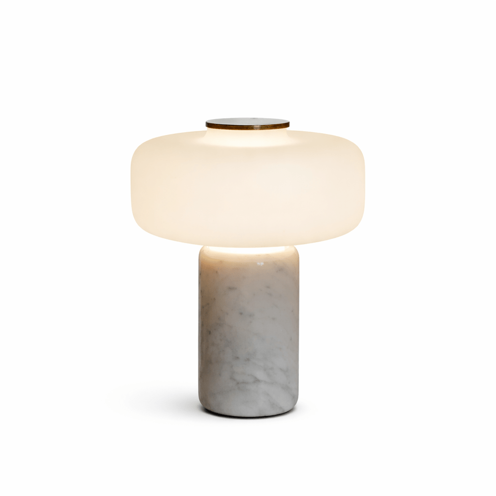 Studio shot of a Clérachic table lamp with a white marble base, its dome shade lit against a plain white background.