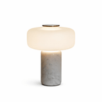Studio shot of a Clérachic table lamp with a white marble base, its dome shade lit against a plain white background.