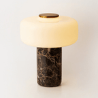 Studio shot of a Clérachic table lamp with a dark marble base and a lit dome shade, isolated on white.