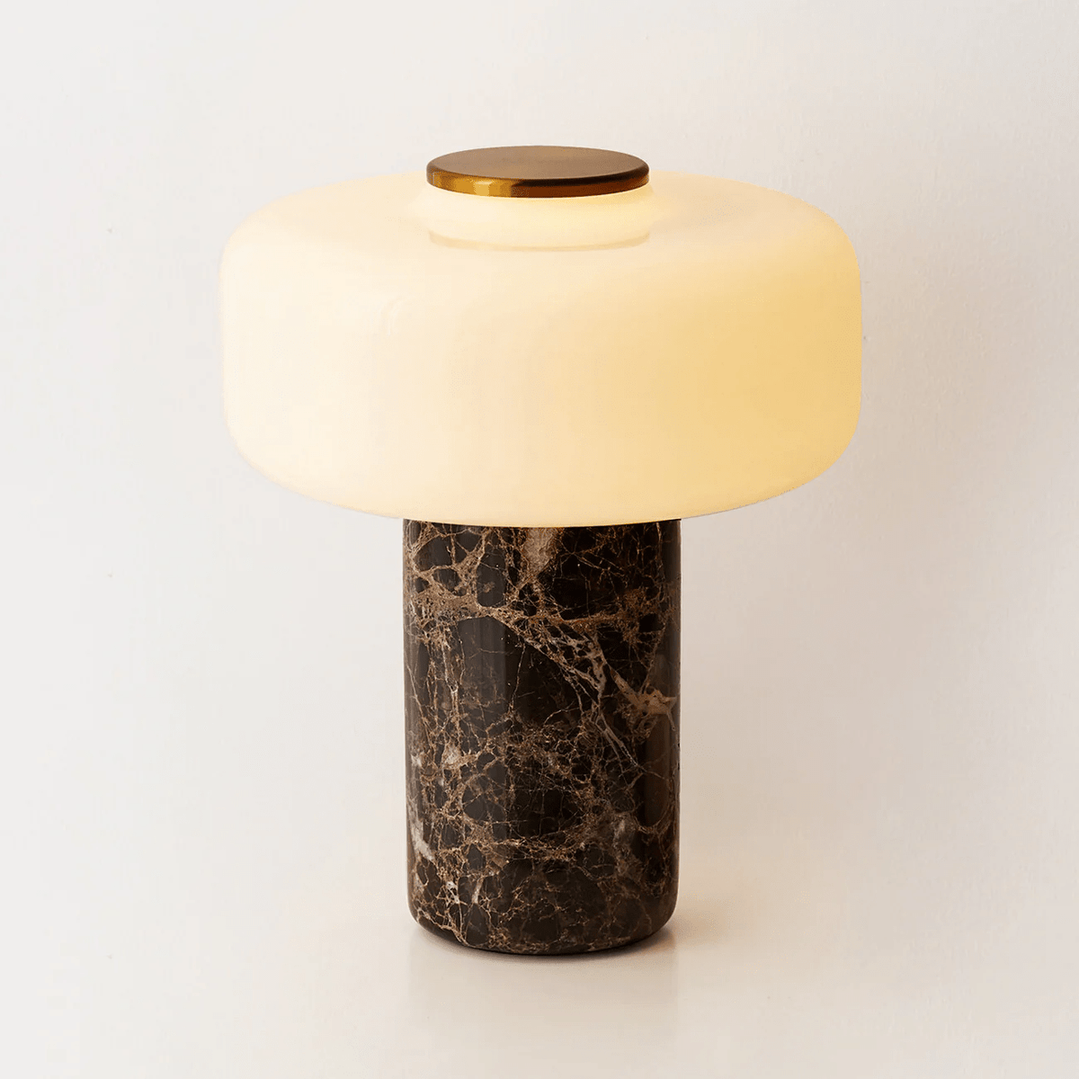 Studio shot of a Clérachic table lamp with a dark marble base and a lit dome shade, isolated on white.