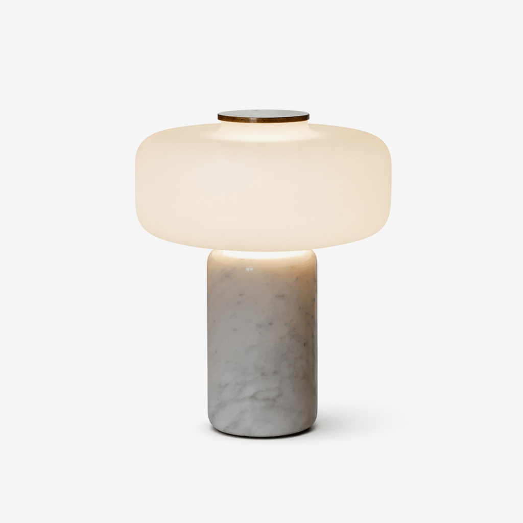 Close studio crop of a Clérachic table lamp with a white marble base, dome shade lit against a soft off-white backdrop.