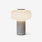 Close studio crop of a Clérachic table lamp with a white marble base, dome shade lit against a soft off-white backdrop.