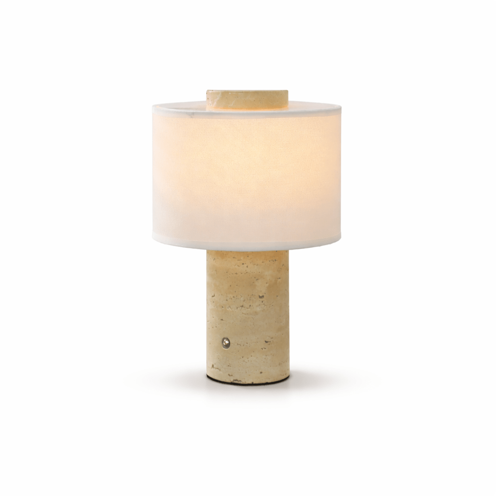 Isolated shot of the Clérachic cordless table lamp with a warm beige travertine base, glowing softly alone.