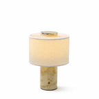 Another angle on the Clérachic table lamp's beige travertine base, isolated against a plain background, lit warm.