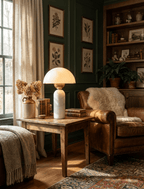 In a dark green library, this Clérachic dome table lamp with a white marble base lights a side table beside a leather armchair.