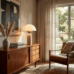 This Clérachic dome table lamp with a travertine base sits lit on a walnut sideboard between pampas grass and abstract art.