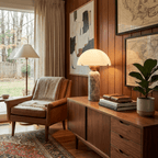 A Clérachic dome table lamp with a travertine base glows on a wood sideboard in a wood-panelled room hung with framed maps.