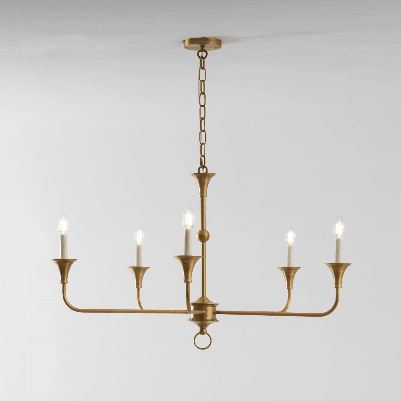 Candle chandelier with slender brass arms and exposed candle-style bulbs, lit in a styled room