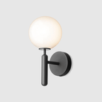 This black Clérachic wall light stands unlit against a plain light grey background, its round white glass globe clearly shown.