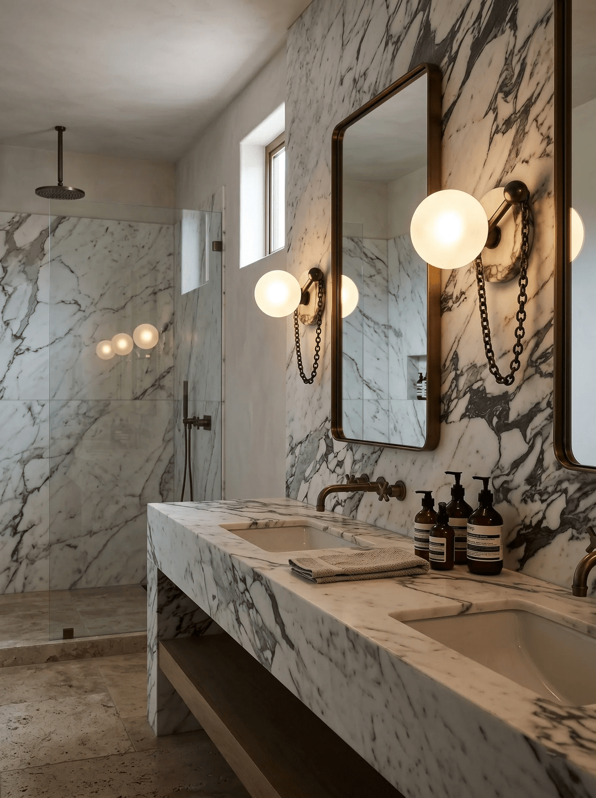 Several Clérachic sconces line a marble-clad bathroom wall beside mirrors, a stone vanity and a walk-in shower.