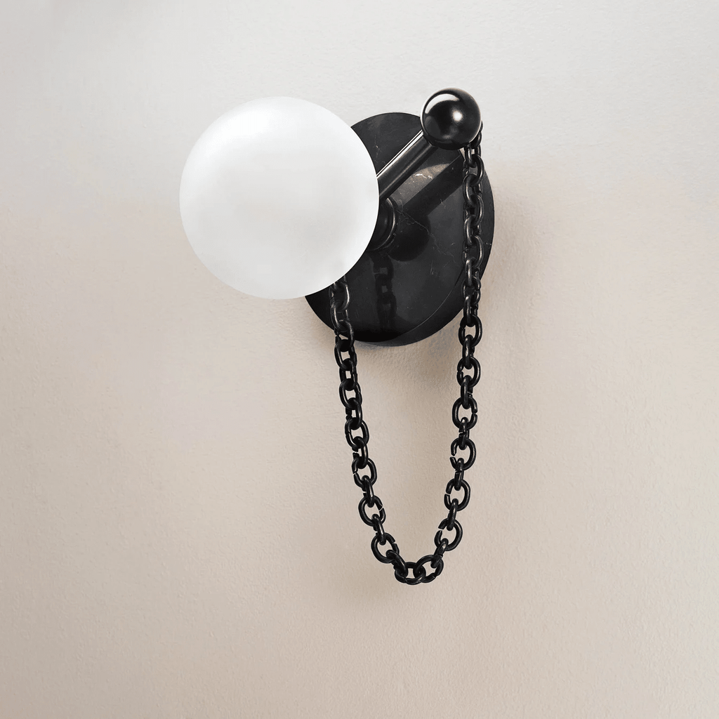 A close-up on plain plaster shows the Clérachic sconce's stone disc, ball finial, frosted globe and hanging chain clearly.