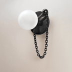 A close-up on plain plaster shows the Clérachic sconce's stone disc, ball finial, frosted globe and hanging chain clearly.