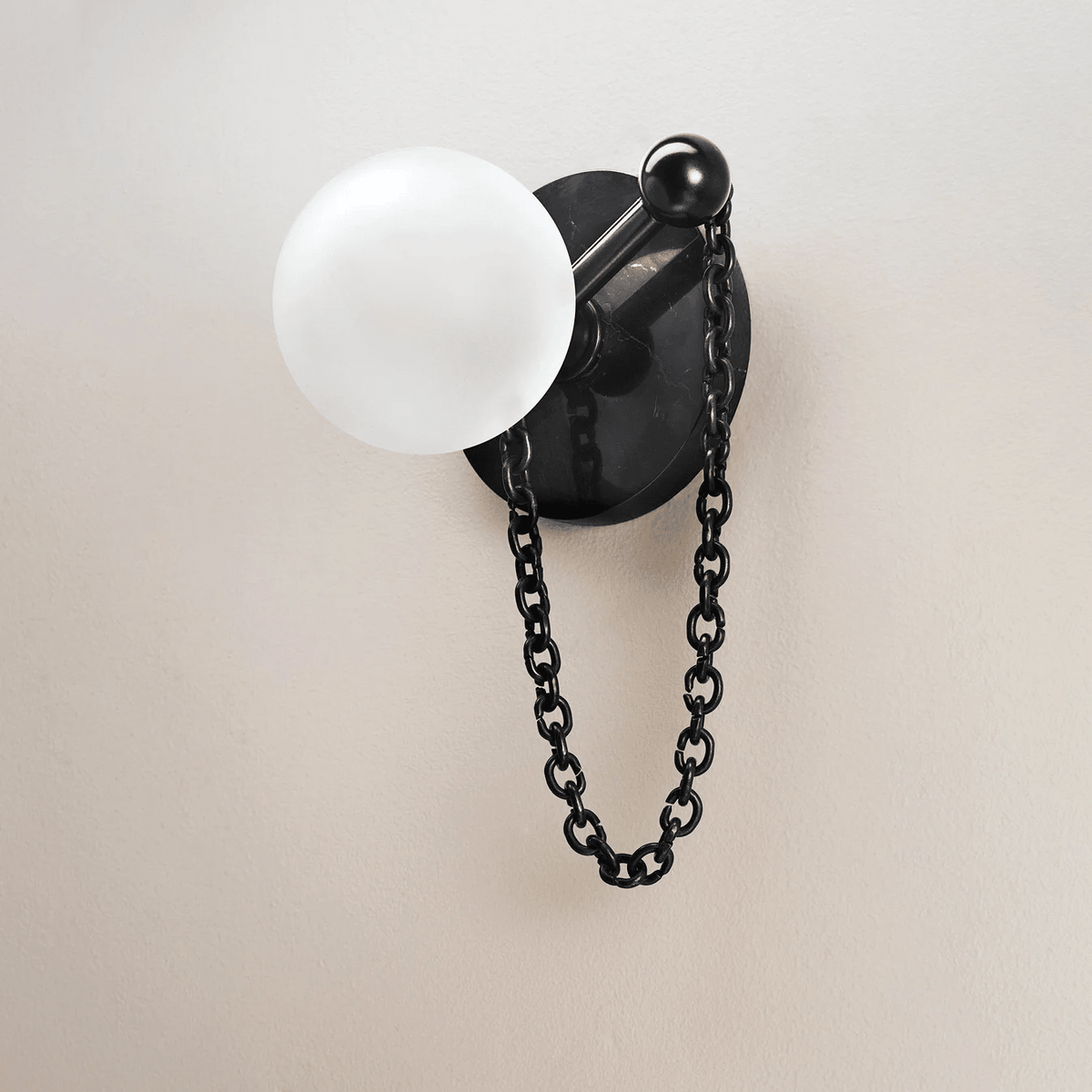 A close-up on plain plaster shows the Clérachic sconce's stone disc, ball finial, frosted globe and hanging chain clearly.