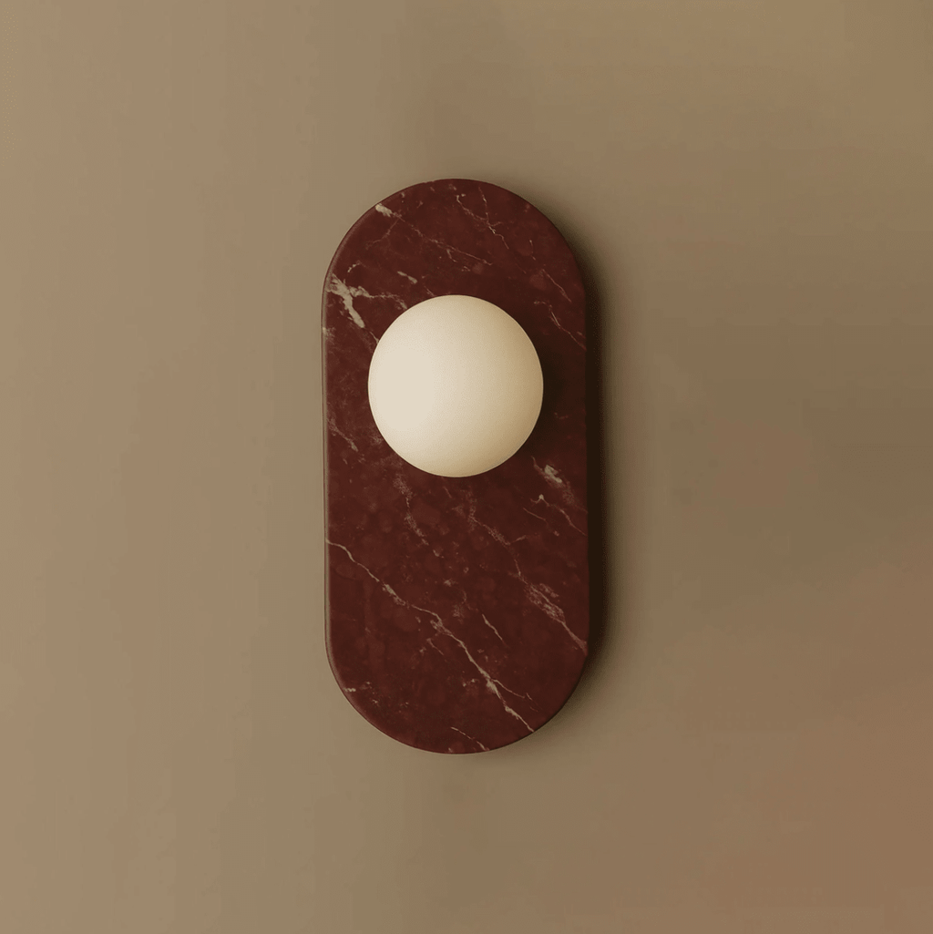 A deep burgundy marble oval holds a frosted glass globe in this Clérachic wall sconce, shown alone against a taupe backdrop.