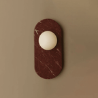A deep burgundy marble oval holds a frosted glass globe in this Clérachic wall sconce, shown alone against a taupe backdrop.
