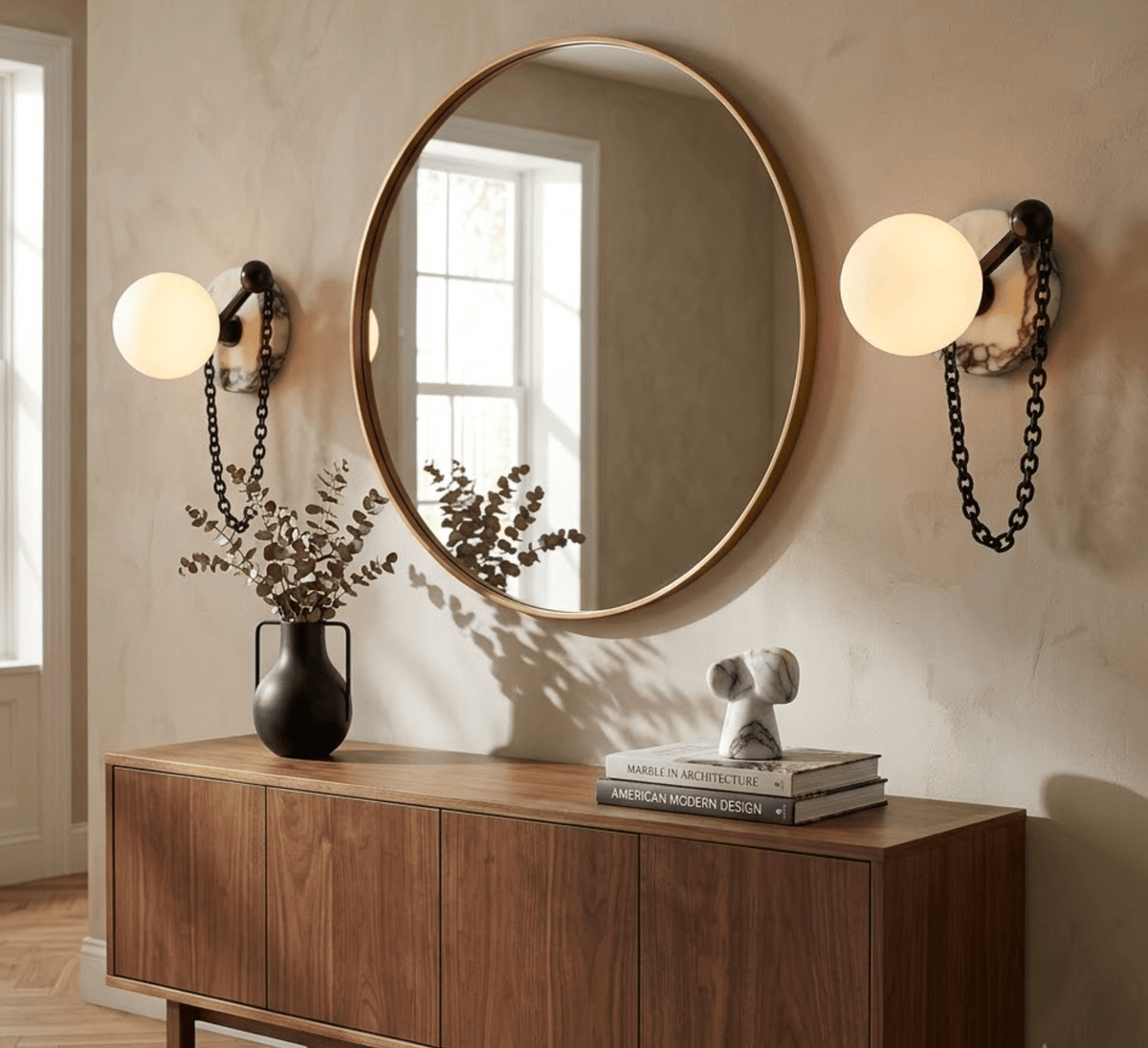 Two Clérachic sconces flank a round mirror over a walnut sideboard, styled with a dark vase and a small dog figurine.