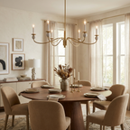 Above a round wood table with a pampas grass arrangement, this Clérachic chandelier in brushed brass lights a room lined with framed art.
