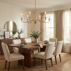 Lit above a wood table set with plates and a vase of greenery, this Clérachic chandelier in brushed brass hangs near a round mirror and sideboard.