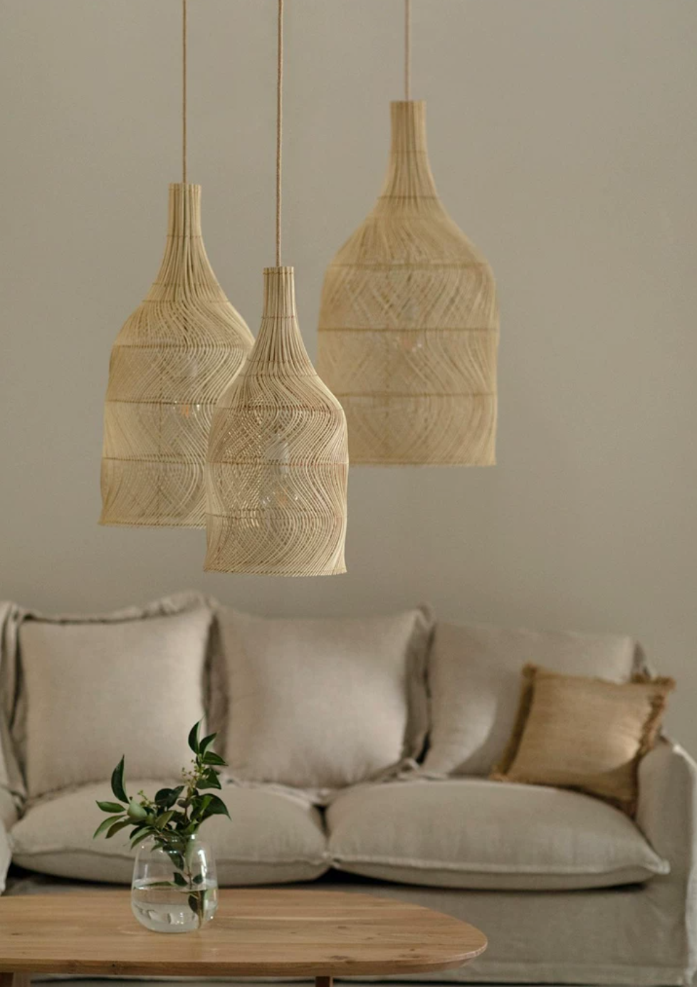 Three sizes of this Clérachic pendant hang together above a linen sofa with a jute cushion and fresh greenery.