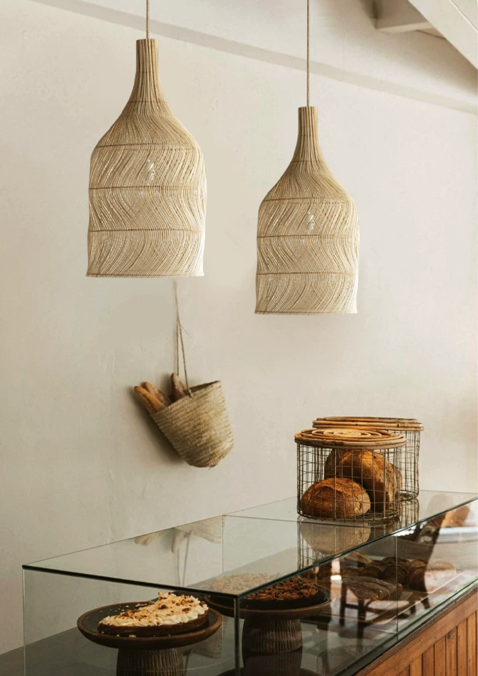 Two of this Clérachic pendant hang above a glass bakery counter with fresh bread and a woven basket.