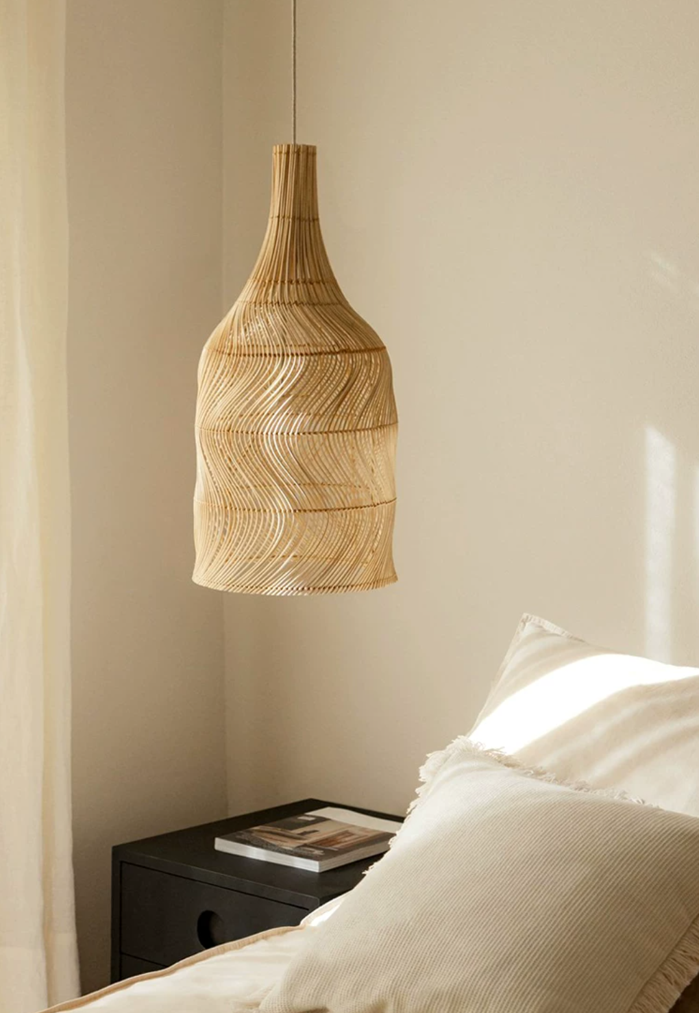 Above a bed with a dark nightstand and cream pillows, this Clérachic pendant hangs in a sunlit corner.