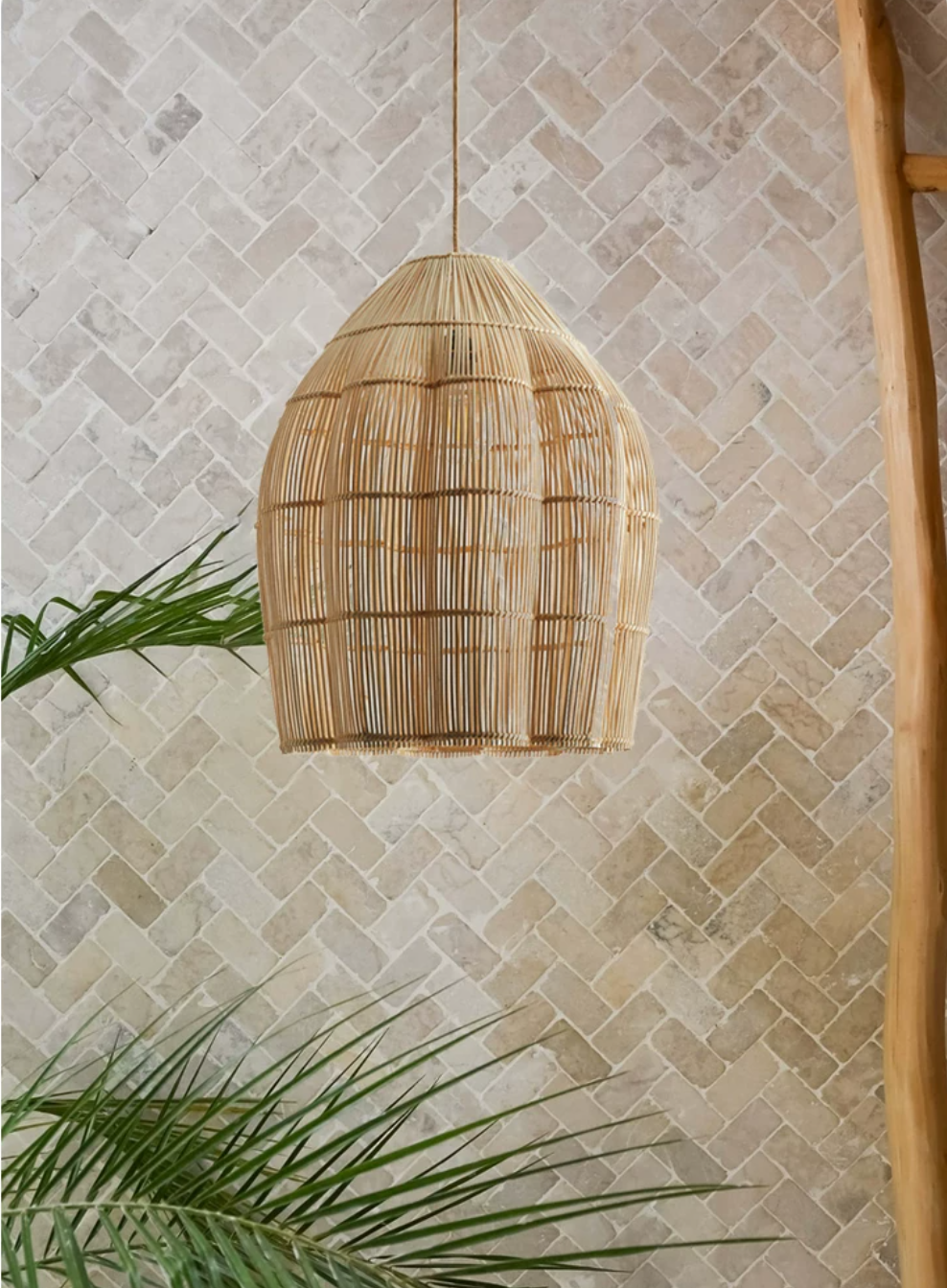 A closer view of this Clérachic pendant's rattan dome against a herringbone stone tile wall.