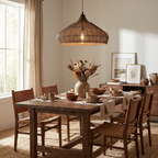 This Clérachic pendant hangs above a wood dining table set with woven placemats, a sideboard of framed art behind.