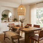 In a dining room with a round mirror, this Clérachic pendant hangs above a wood table set with woven leather chairs.