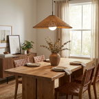 Woven leather chairs surround a wood table set beneath this lit Clérachic pendant near a curtained window.