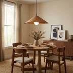 This Clérachic pendant lights a round dining table set beside a sideboard with framed art.