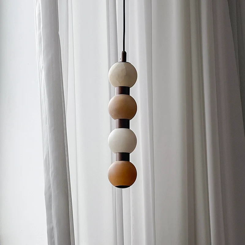 Close view of four pale alabaster spheres at the top of this Clérachic pendant against a curtain.