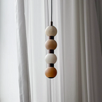 Close view of four pale alabaster spheres at the top of this Clérachic pendant against a curtain.