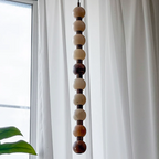 This Clérachic pendant's pale and tan spheres hang in daylight, reaching toward a monstera leaf below.