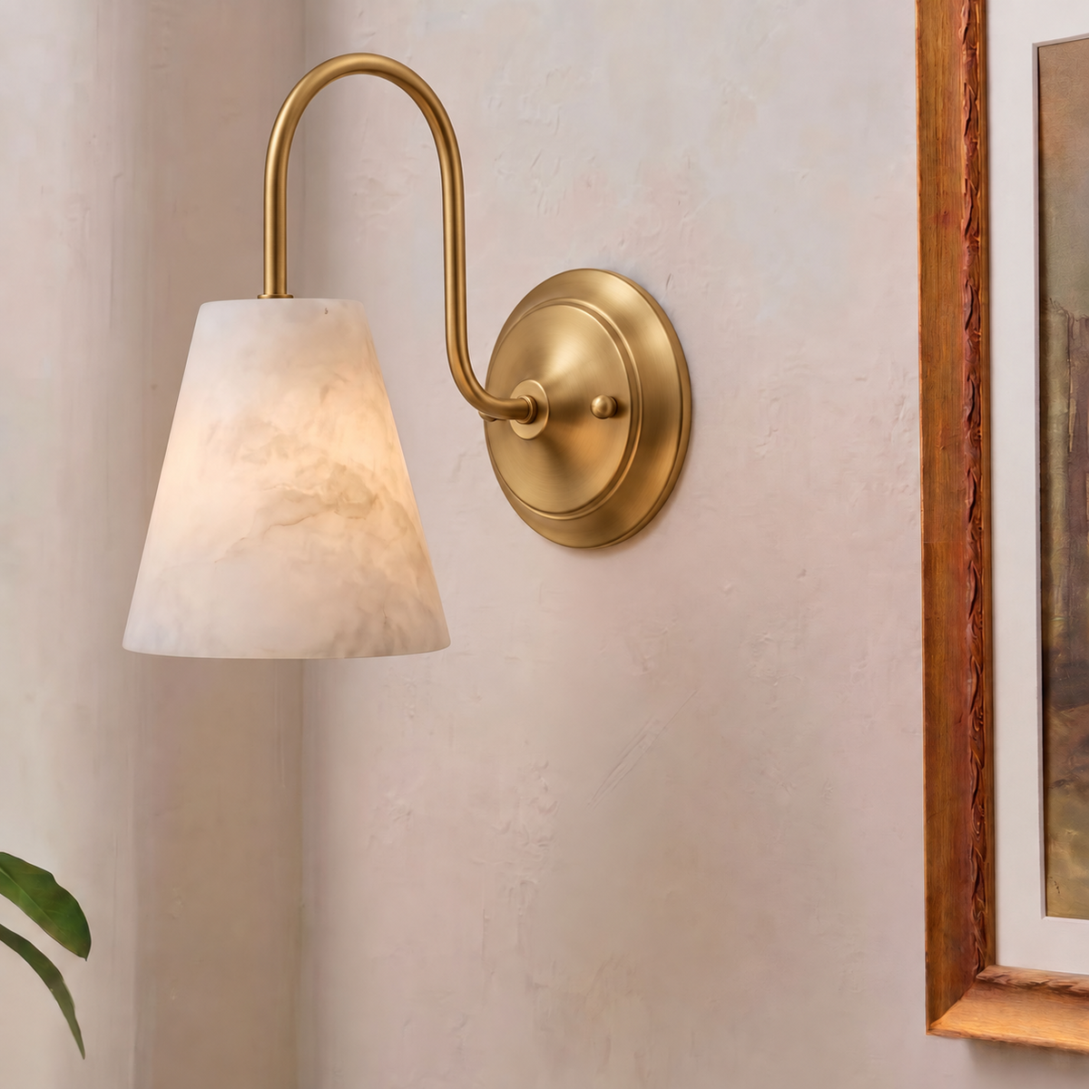 In brushed brass, this Clérachic wall sconce sits unlit beside a framed painting, its gooseneck arm arcing over the shade.