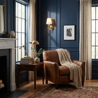 Against a deep navy panelled wall, this brushed brass Clérachic wall sconce glows beside a marble fireplace and leather armchair.