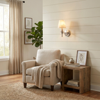 On a shiplap wall, this matte black Clérachic wall sconce glows beside a fiddle-leaf fig plant and cream armchair.