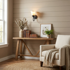 On a shiplap wall, this matte black Clérachic wall sconce glows above a wooden bench beside a cream armchair.