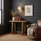 Mounted on dark shiplap panelling, this Clérachic wall sconce in brushed nickel lights a console beside a leather armchair.