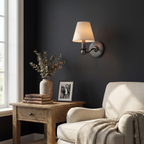 Against a deep navy wall, this matte black Clérachic wall sconce lights a side table beside a cream armchair.