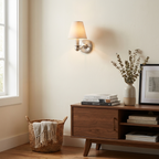 This brushed nickel Clérachic wall sconce glows above a walnut console with a woven basket and stacked books.