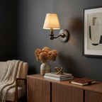 On a charcoal wall, this matte black Clérachic wall sconce glows above a sideboard dressed with dried flowers and books.