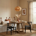A pumpkin-round rattan Clérachic pendant glows above a round table with black wishbone chairs and bench seating.