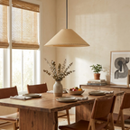 Beneath bamboo window blinds, a beige Clérachic pendant lights a rustic wooden dining table.