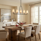 Against cream walls with sheer curtains, this Clérachic chandelier in matte black hangs over beige upholstered dining chairs.