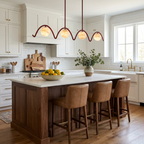 Above a wood island with brown leather stools, this Clérachic chandelier arches over the counter in matte red.