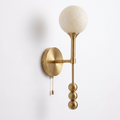 Studio shot of this Clérachic wall sconce in brushed brass, alabaster shade lit softly above the pull chain.