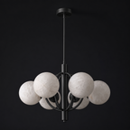 Studio shot of this Clérachic chandelier in matte black, its alabaster shades caged within intersecting rings.